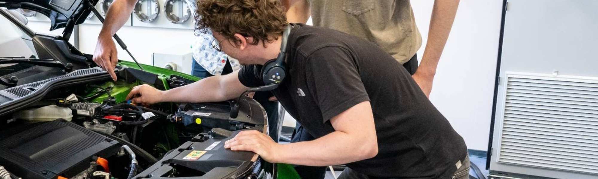 Studenten en docent automotive kijken naar de motor van de auto.