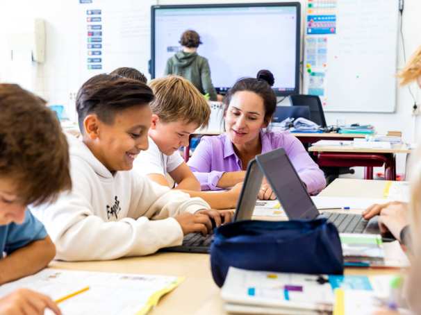 De lerares van de opleiding leraar basisonderwijs legt iets persoonlijk uit aan een leerling aan zijn tafel.