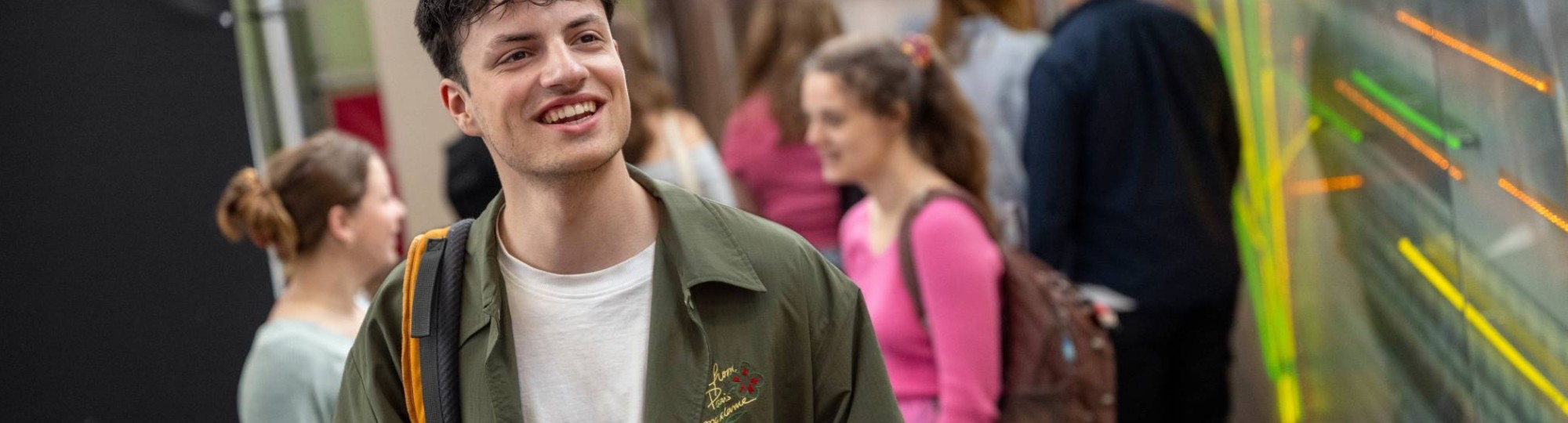 Student staat in de gang met de rugzak op de rug, in de lichtstraat van gebouw R26.