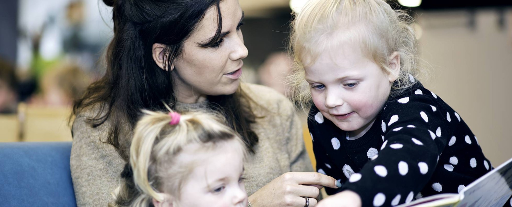 Vrouw laat aan twee kinderen een boek zien.