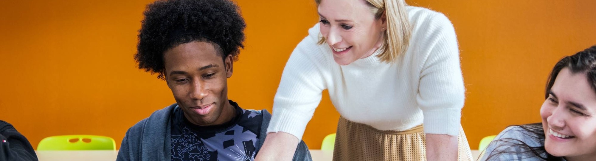 docent wijst lachend op laptop bij twee masterstudenten