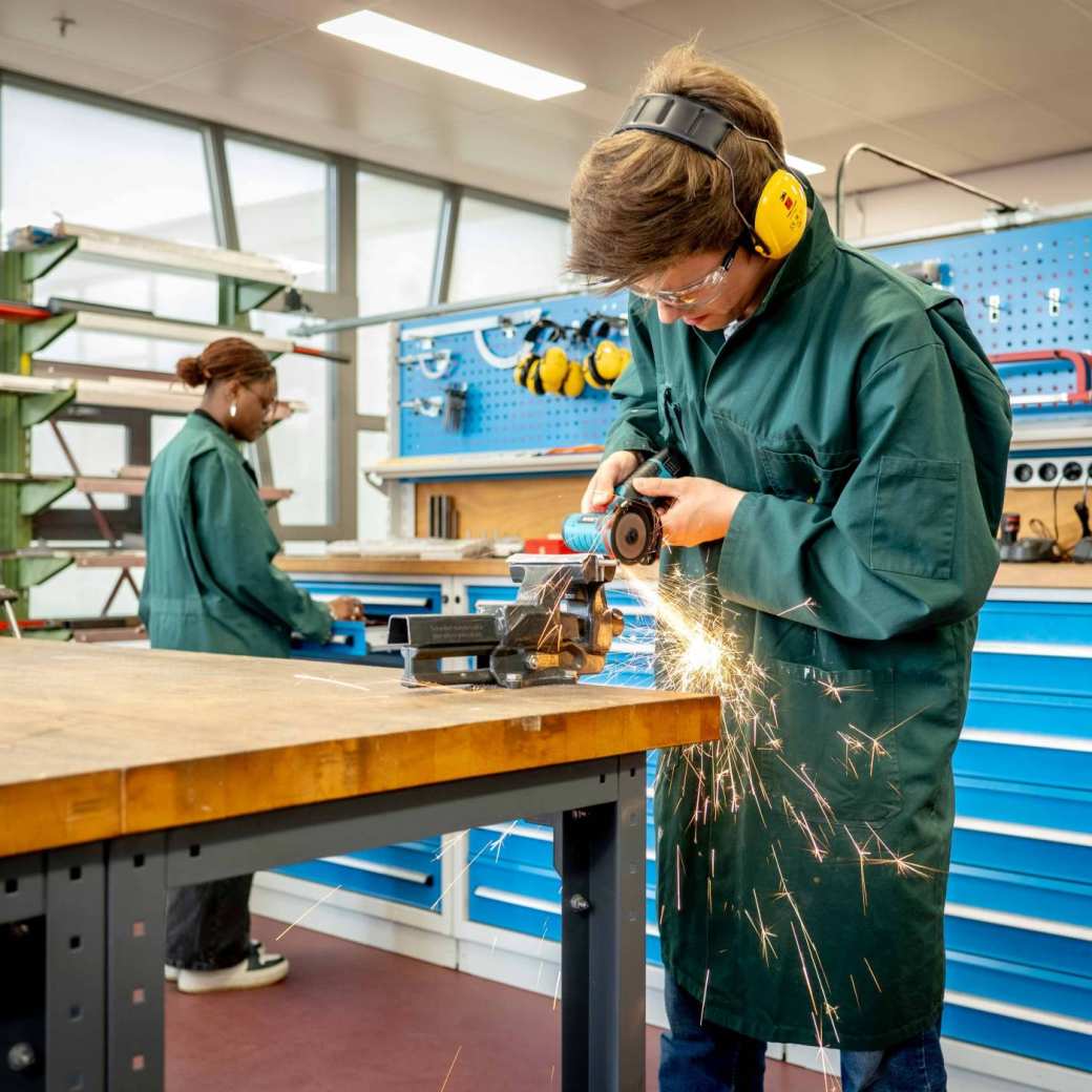 Een werktuigbouwkunde student slijpt een metalen staaf op maat.