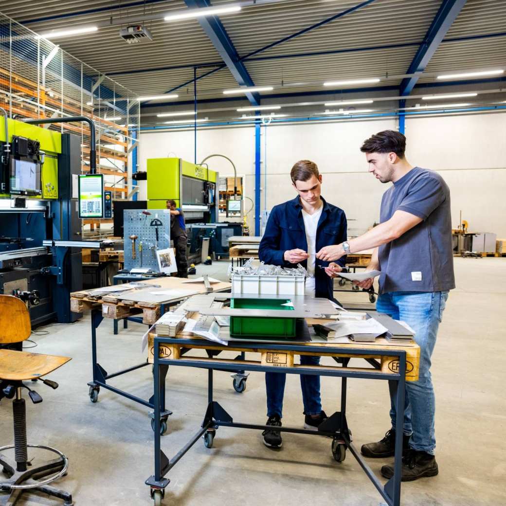 Twee studenten Technische Bedrijfskunde overleggen op de werkvloer.