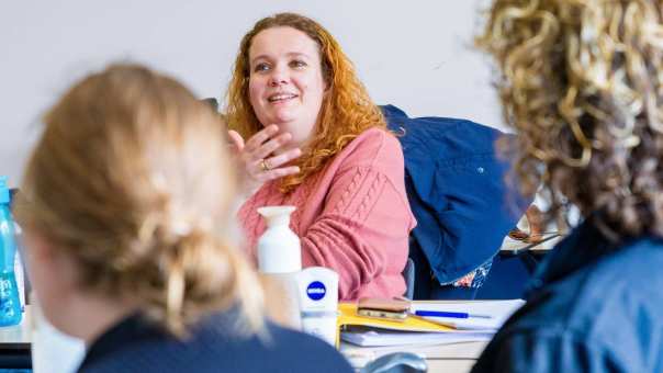 Vrouw in roze trui is in gesprek met docent tijdens de cursus acute pijn service.