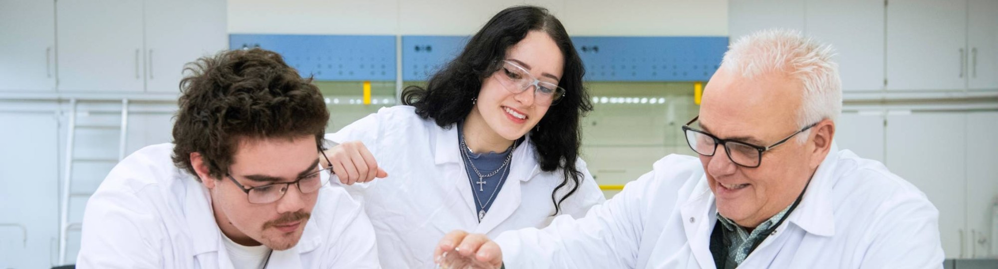 Twee Leraar Scheikunde studenten voeren een proef uit met een docent scheikunde.