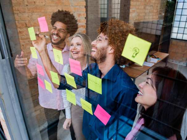 Groep jonge mensen plakken post-its op een glazen wand in een kantoor
