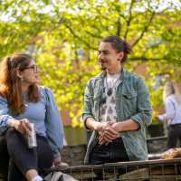 Twee studenten lachen naar elkaar, zijn buiten bij K33. 