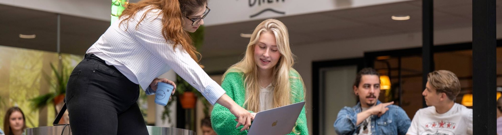 Twee studenten overleggen samen en wijzen naar de laptop, aan het werk bij The Brew.