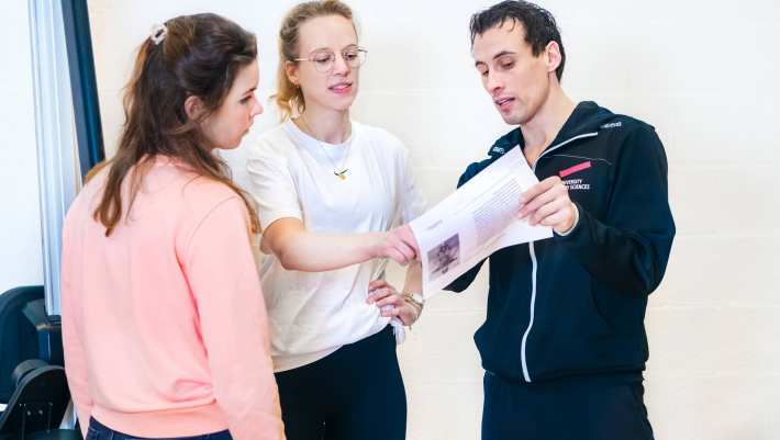 Docent helpt studenten en legt wat uit met behulp van een blaadje. 