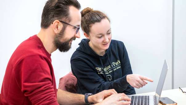 Vrouwelijke student wijst op de computer van een mannelijke student.