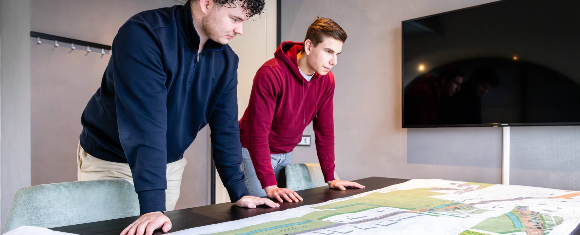 Twee mannen leunen op een bureau met daarop een omgevingskaart.