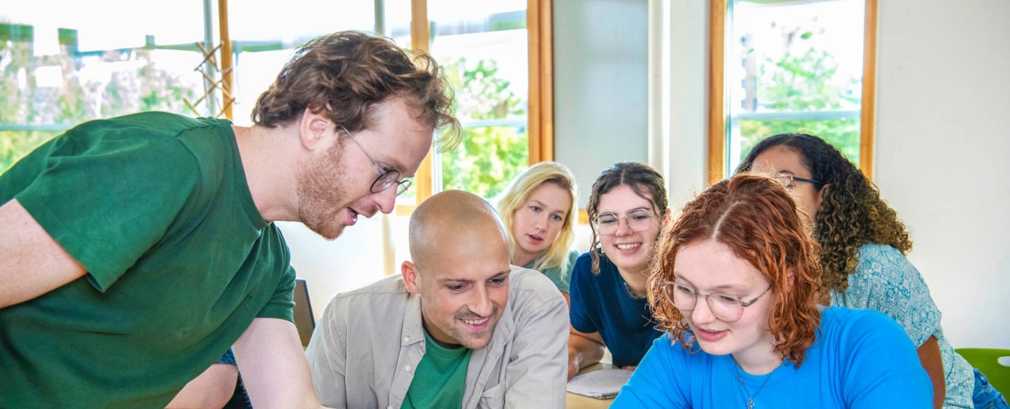 Docent wijst iets aan op de laptop van twee studenten