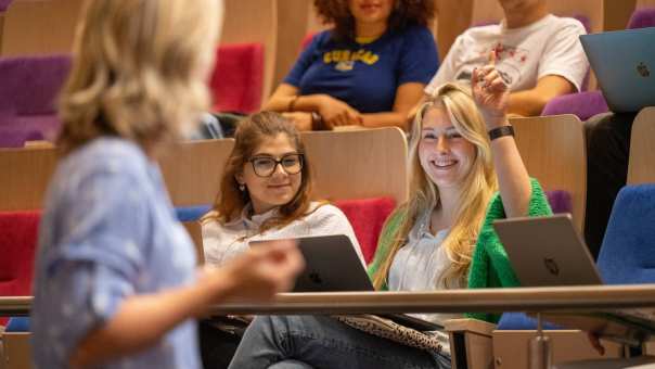 Studente steekt hand op tijdens hoorcollege in de collegezaal