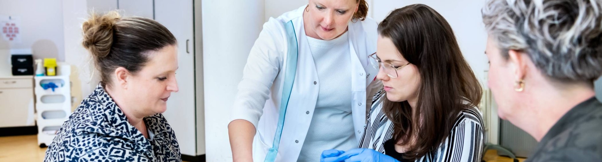 Docent geeft aan 3 studenten uitleg over wondverzorging tijdens les Verpleegkunde deeltijd