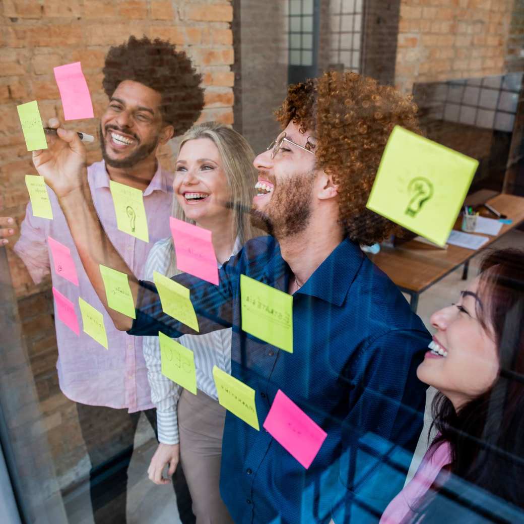 Groep jonge mensen plakken post-its op een glazen wand in een kantoor
