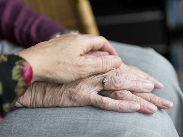 handen oudere en verzorger in beeld