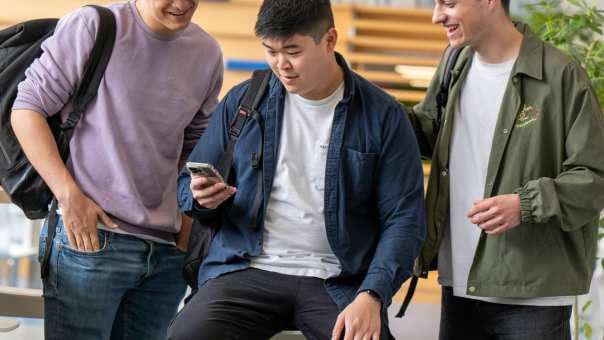 3 studenten/jongens kijken op hun mobiel en lachen