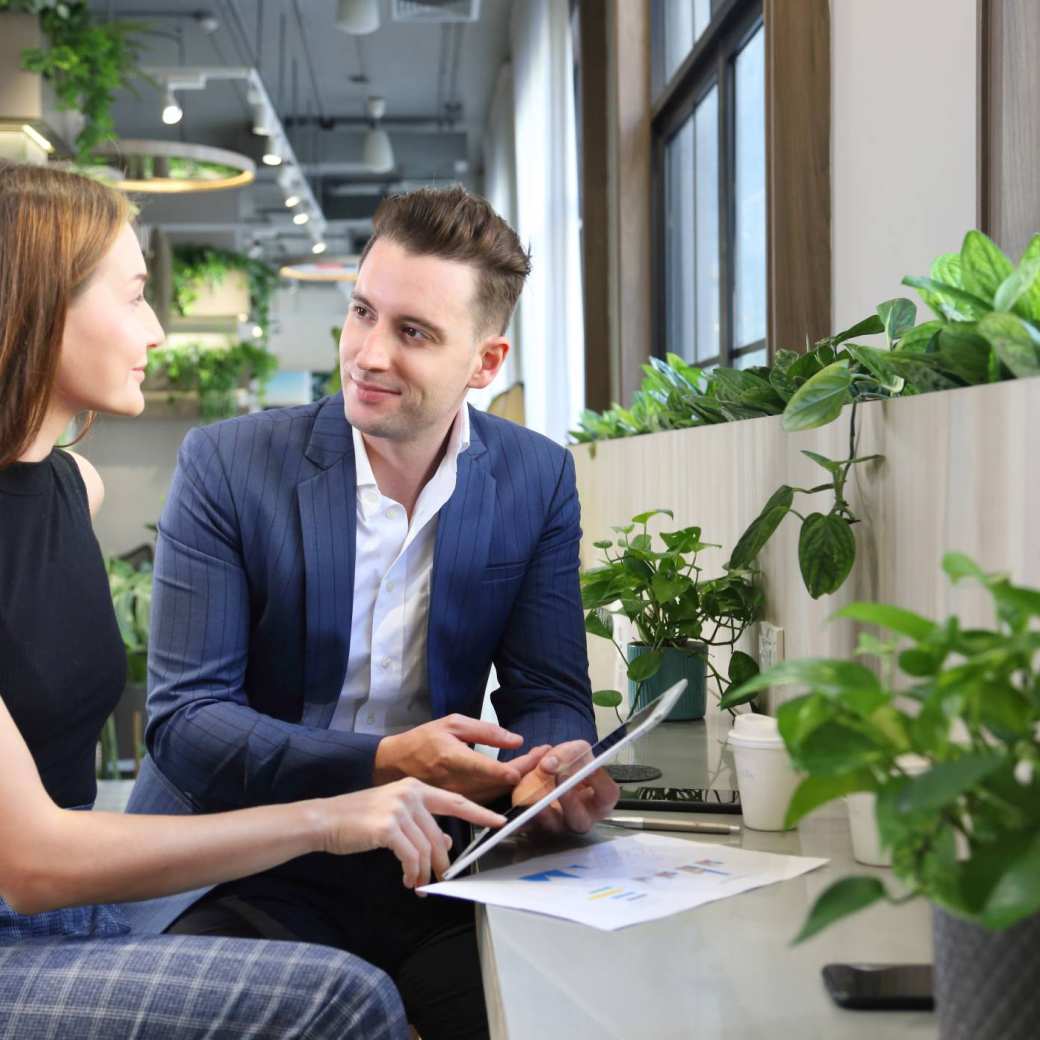 Foto van twee mensen in overleg met een tablet in kantoorruimte met planten voor projectpagina van het ass. lectoraat Sustianable Finance & Tax.