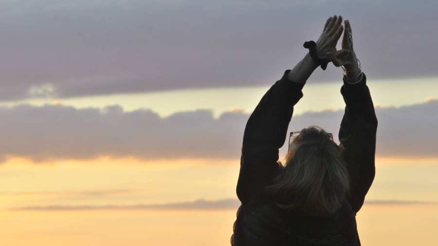 Een dame steekt haar handen in de lucht tijdens een zonsondergang.