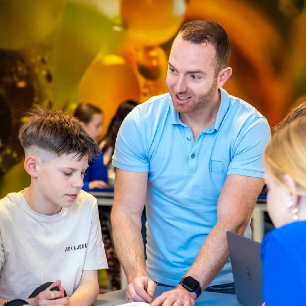 Docent Niels Janssen geeft uitleg aan 2 leerlingen door middel van een boek op het Citadel College. 