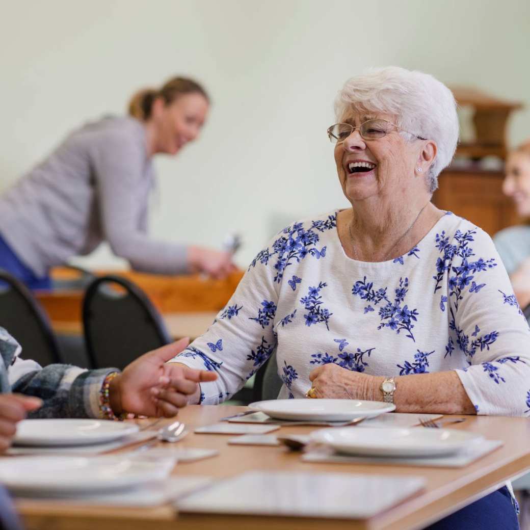 Lachende oudere vrouw in gesprek met andere mensen met wit met blauwe top