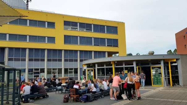 Studenten komen na de lessen samen bij Lokaal 99 om iets te drinken. Op de achtergrond het onderwijsgebouw van Engineering en Automotive.