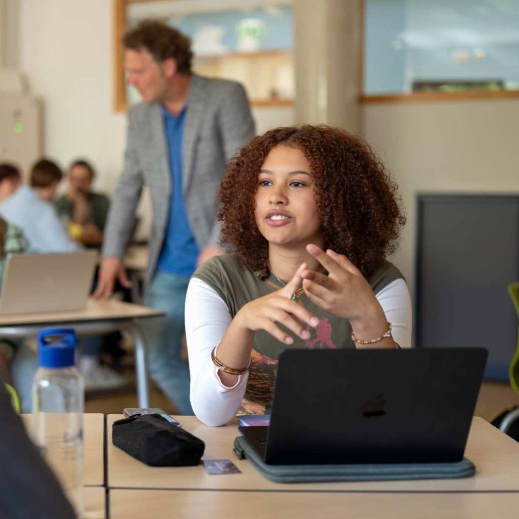 Meisje student in gesprek met jongen, in de klas, met laptop.