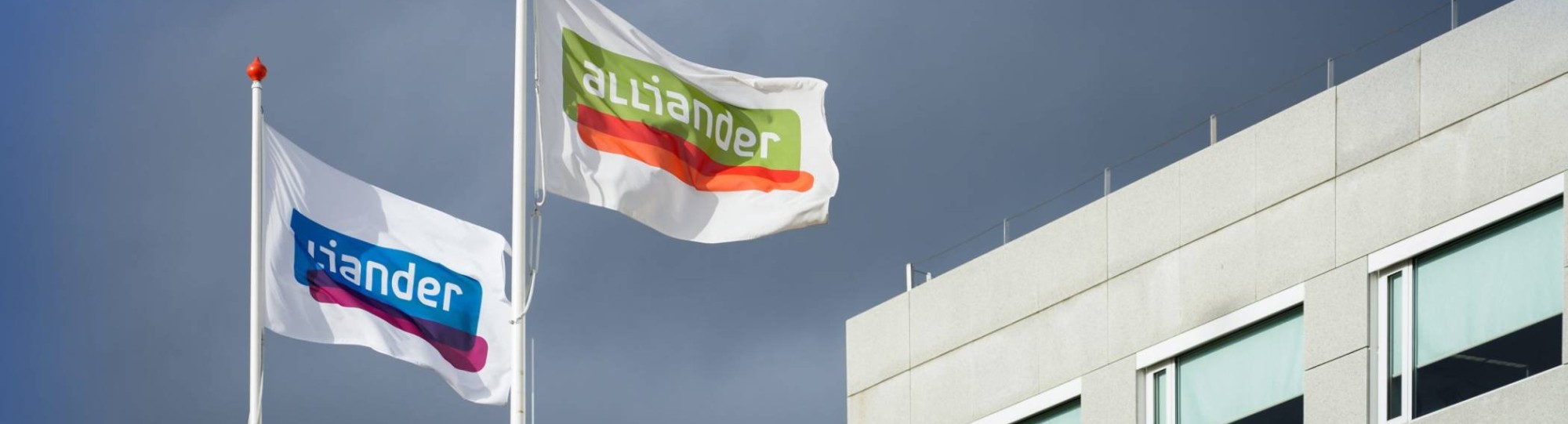 De vlag van Alliander wappert voor een gebouw. Seece