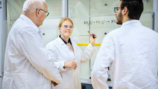 Een student laat een formule zien aan de docent en een student.
