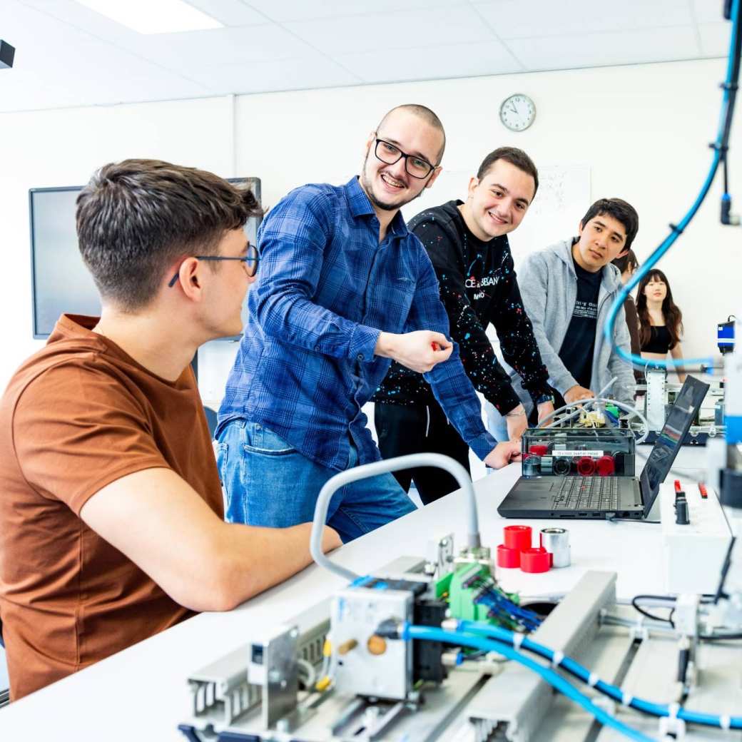 Docent en studenten elektrotechniek  aan een Programmable Logic Controller (PLC).