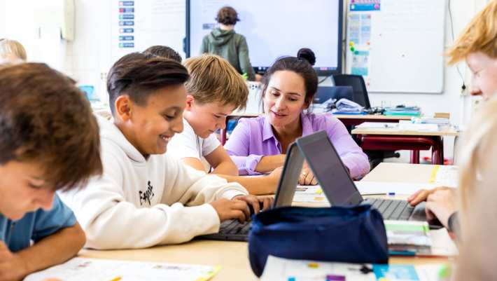 De lerares van de opleiding leraar basisonderwijs legt iets persoonlijk uit aan een leerling aan zijn tafel.