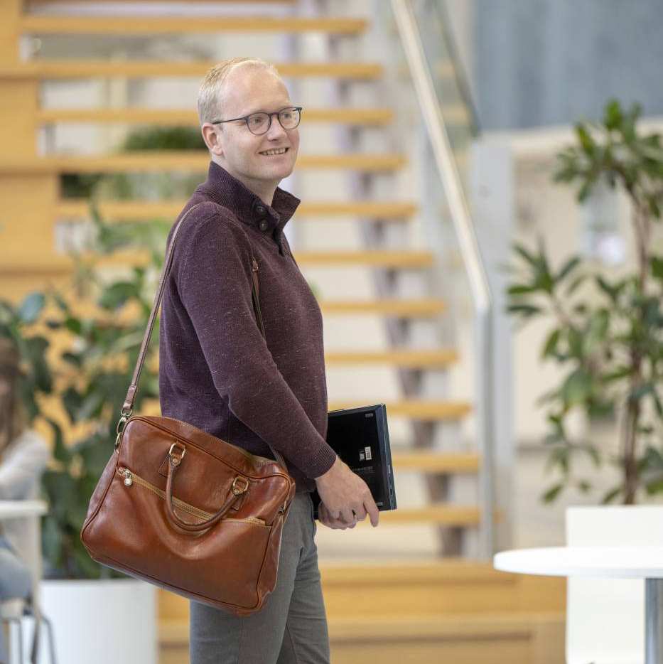 Mannelijke student loopt lachend door het schoolgebouw met tas en laptop