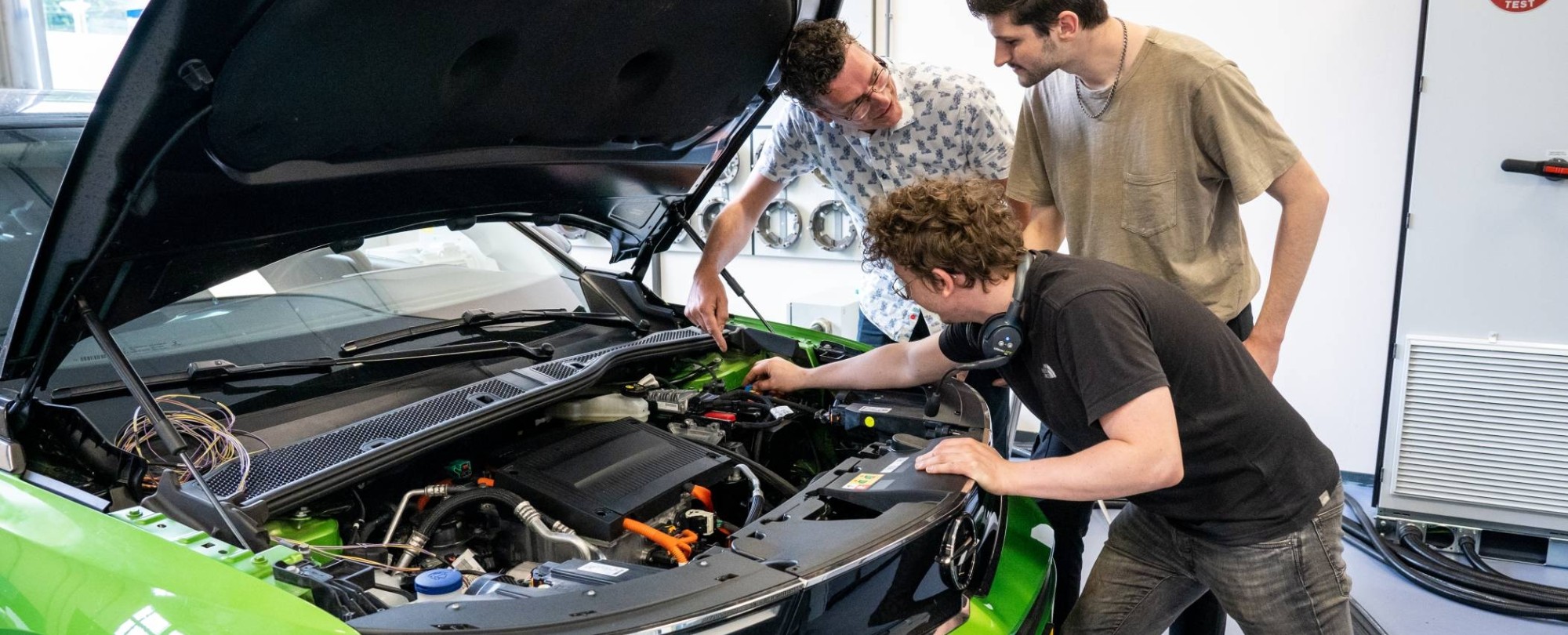 Studenten en docent automotive kijken naar de motor van de auto.